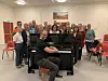 NYT PIANO. Her sitter Sveinar Aase foran det nye pianoet på Røsvik samfunnshus, med koret Sangria i bakgrunnen. Det skal være innvielseskonsert for pianoet søndag 1. september der blant andre disse deltar.