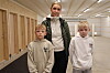 Tre personer står i en lys innendørs hall med tredører og skytebane i bakgrunnen.